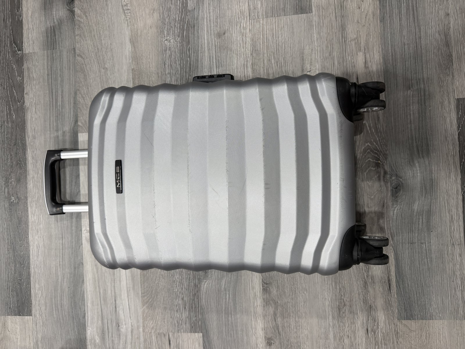 Valise rigide argentee MCS fermee, coque nervuree, quatre roues et poignee telescopique