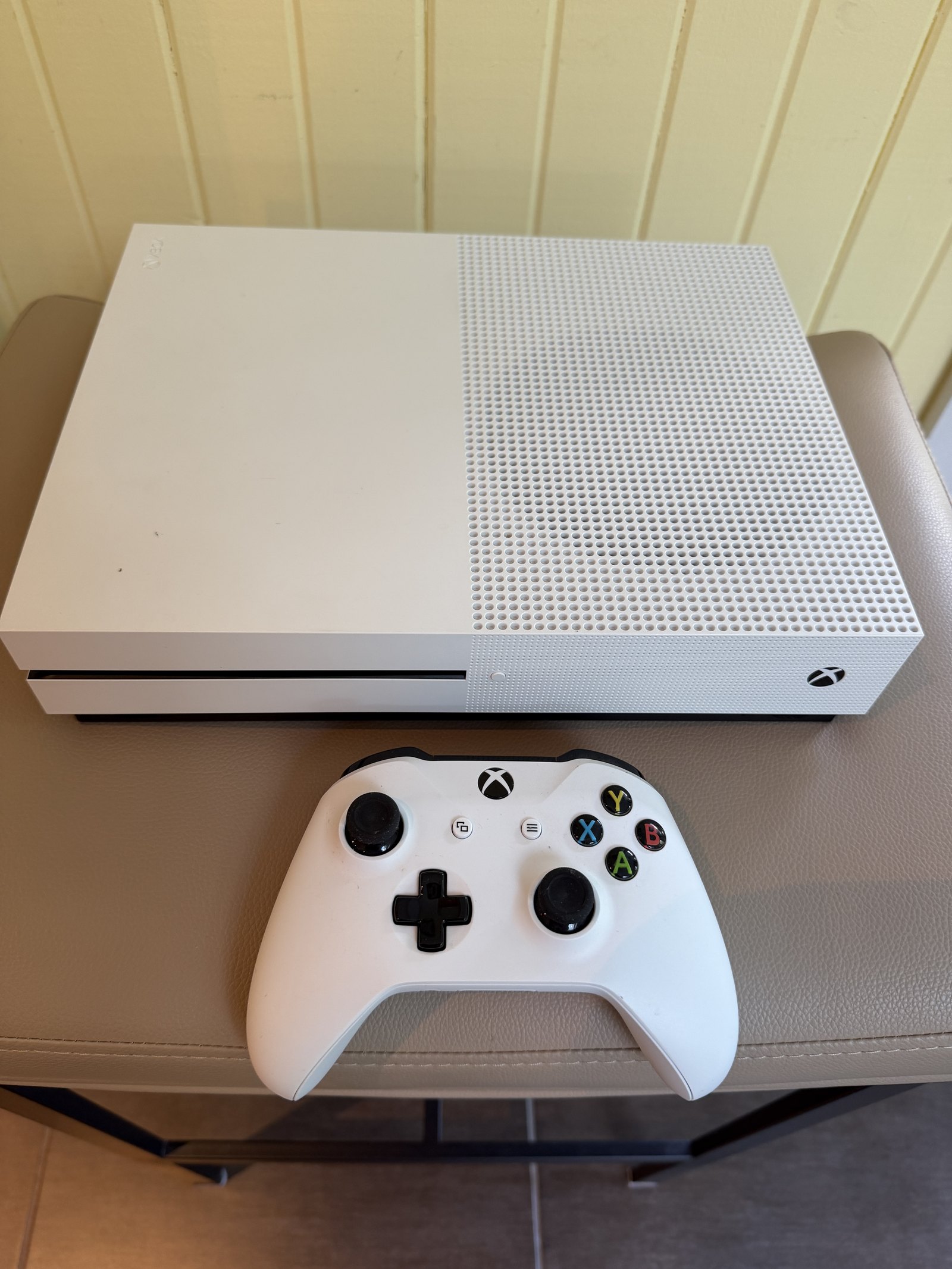 Console Xbox One S blanche debout, sa manette sans fil blanche posee a cote